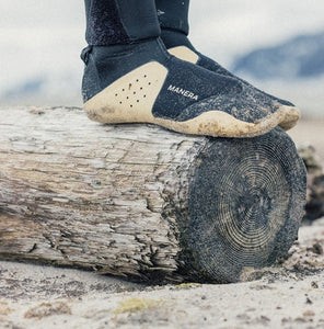 Close up of surfing booties being worn by a person standing on a log